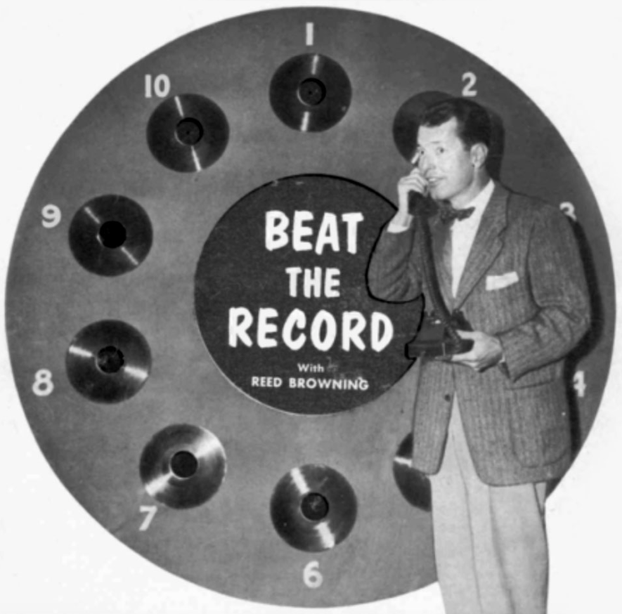 Photo of ABC radio host Reed Browning in front of a display for Beat the Record containing 10 vinyl records