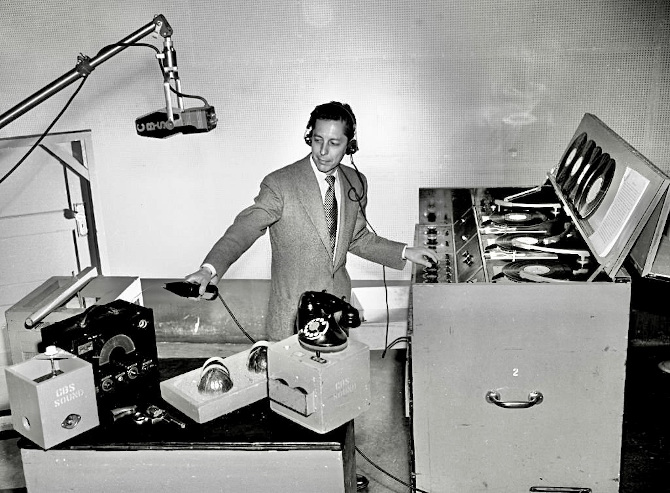 Photo of CBS sound technician Cliff Thorsness working to produce sound effects during a program in Hollywood on July 1952. He's well-dressed in a coat and tie with headphones on.