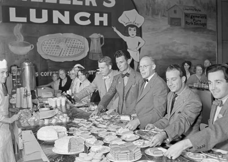 Chester Lauck and Norris Goff at the Indiana State Fair in 1935, where they performed as Lum and Abner. The photo shows Lauch, Goff, their friend Jerry Hausner and others standing in a cafeteria line choosing plates of food.